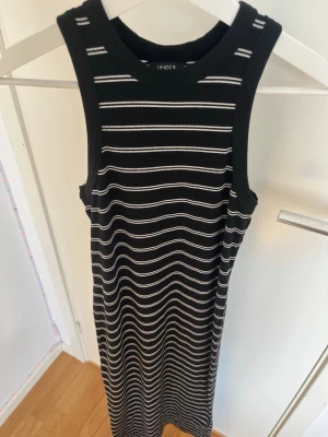 Svartvit randig långklänning  - Svart långklänning från Lindex med vita horisontella ränder. Klänningen är ärmlös och har en rund halsringning. Materialet är ribbat och stretchigt vilket ger en bekväm passform. Perfekt för dig som gillar en enkel men snygg stil.