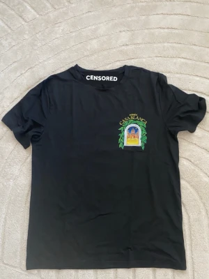 Svart Casablanca t-shirt med tryck - Snygg svart t-shirt från Casablanca med färgglatt tryck av ett fönster och gröna blad på bröstet och ryggen. Texten 'Avenida Casablanca' syns tydligt. Klassisk passform och rund hals, perfekt för en trendig streetwear-look.