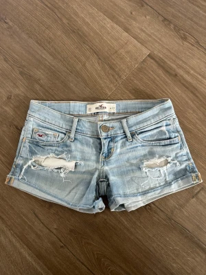 Ljusblå slitna jeansshorts Hollister - Ett par ljusblå jeansshorts från Hollister med slitna detaljer och råa kanter. Klassisk femficksmodell med låg midja och knappgylf. Perfekta för sommaren och ger en avslappnad vibe🌺🤍