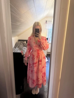 Rosa långklänning - Rosa blommig långklänning med knappar framtill, liknar adoore. Superfin till mösspåtagning eller midsommar!                                                        Köptes på vinted men säljs då den är lite för liten för mig.