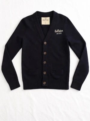 Mörkblå kofta från Hollister - Kofta i svart från Hollister med broderad logga och text 'Hollister 1922' på bröstet. V-ringad modell med fem knappar framtill och två fickor. Ribbstickade muddar vid ärmslut och nederkant. Perfekt för lager på lager och enkel att matcha. Om ni har några frågor skriv gärna!🙌 fraktar direkt😊💯