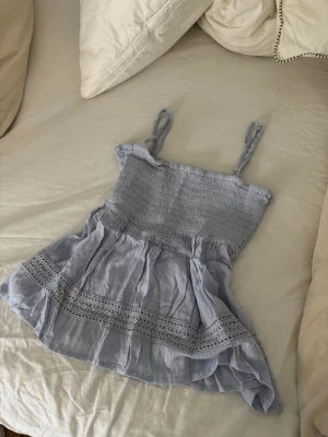 Ljusblå linnetopp med spetsdetaljer - Supersöt ljusblå linnetopp med smockad överdel och tunna axelband. Toppen har volangkant och fina spetsdetaljer längst ner. Perfekt för varma dagar och ger pil, chill vibe till din outfit.