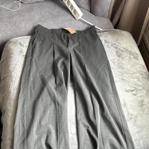 Grå kostymbyxor med pressveck - Snygga grå kostymbyxor med raka ben och klassiskt pressveck. Byxorna har hög midja, två fickor bak och stängs med dragkedja och knapp. Perfekta för en stilren och modern look. Endast testade orginalförpackning finns kvar, samt prislappar. Storlek är Loose, så förvänta dig det också. Nypris ca 1200 kr