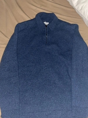 Blå halvzip tröja med krage - Mysig blå tröja med halvzip och ståkrage. Tröjan har långa ärmar och ribbade muddar vid ärmslut och nederkant. Perfekt för lager på lager och enkel att matcha med jeans eller chinos.