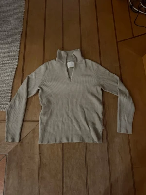 Stickad tröja - Snygg beige ribbad tröja med hög krage och halv dragkedja framtill. Långärmad modell i mjukt material som passar perfekt till jeans eller kjol. Enkel och stilren design som är lätt att matcha.