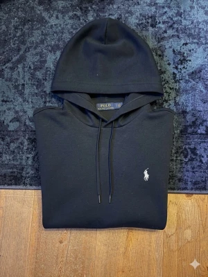 Svart hoodie från Polo Ralph Lauren - Hej!👋  Säljer en svart/mörkblå hoodie från Polo Ralph Lauren. Mycket bra skick, men är lite nopprig (främst på en av ärmarna), men inget som riktigt syns vid användning. Det noppriga är nog väldigt möjligt att få bort med maskin eller för hand om man orkar. Storlek S. Finns qr-kod som man kan skanna för att se till att den är 100% äkta!😀 Hör av er vid frågor!💯