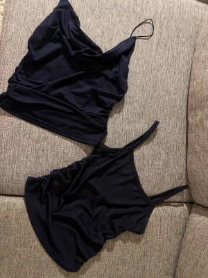 Två marinblåa toppar  - Säljer två marinblåa toppar med tunna axelband. Ena toppen har en draperad halsringning och den andra har en klassisk rak skärning. Perfekta att matcha med jeans eller kjol för en enkel och stilren look. Använda fåtal gånger!💕 köpta i en butik i Italien💕