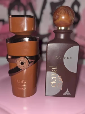 Två parfymer set - Två unika parfymflaskor i bruna nyanser. Den ena flaskan heter Eternal Coffee och har en marmorerad rund kork, medan den andra heter Just Oud Choco och har en asymmetrisk design med dekorativt band. Båda flaskorna är tillverkade i glas och har eleganta detaljer i guld.