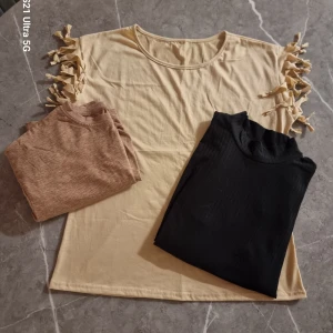 Paket med 3 toppar!  - Säljer en svart ribbad polotopp med trekvartsärm. Toppen har en smickrande passform och är perfekt för att styla med jeans eller kjol. Materialet känns mjukt och stretchigt, vilket gör den bekväm att bära hela dagen. En beige topp med fransar uppe på ärmarna samt en lite mörkare beige tshirt 