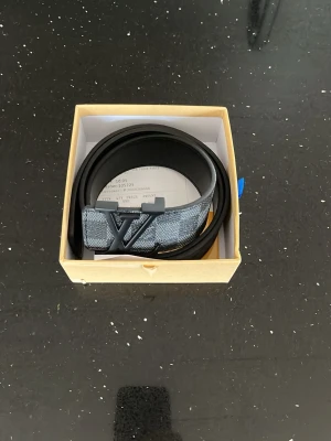 Svart hm bälte  - Snyggt svart bälte från hm  med klassiskt hm  i mörk metall. Bältet har en diskret grå detalj med rutigt mönster vid spännet och är gjort i exklusivt skinn. Perfekt accessoar för att lyfta din outfit.