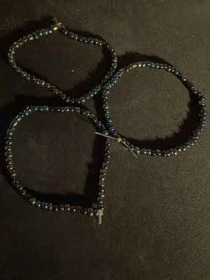Tre armband med mörka pärlor - Säljer tre handgjorda armband med små, mörka pärlor i blå och lila toner. Armbanden har en enkel och stilren design med elastisk tråd som gör dem lätta att ta på och av. Perfekta för att addera en subtil färgklick till din outfit.OBS! Materialet är okänt, kan ej garantera att det är rostfritt.