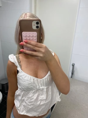 Vit linnetopp med spetsdetaljer - Säljer en söt vit linnetopp med breda axelband och fina spetsdetaljer. Toppen har en luftig och lös passform, perfekt för varma dagar. Materialet känns lätt och toppen har en feminin v-ringning. Passar perfekt till jeans eller kjol!