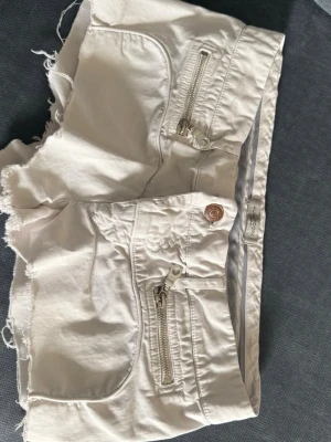 Vita shorts med dragkedjor - Säljer ett par vita shorts med råa kanter och två snygga dragkedjor framtill. Shortsen har knappstängning och fickor både fram och bak. Perfekta för sommaren och riktigt sköna att bära.