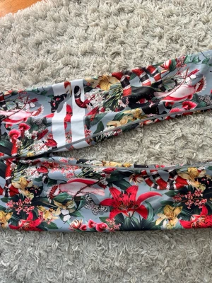 Mönstrade leggings från Stronger - Säljer ett par leggings från Stronger med färgglatt blommönster och inslag av fjärilar och ormar på ljusgrå botten. Materialet är stretchigt och passar perfekt för träning eller chill. Midjan är normalhög och tyget känns mjukt mot huden.
