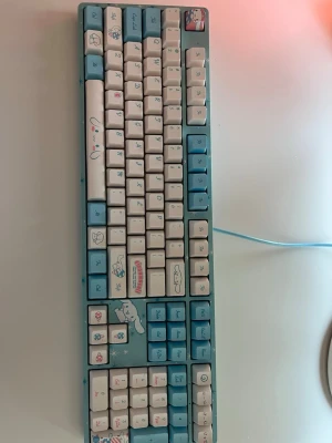 Cinnamoroll tangentbord blå/vit 100% 5108S mekaniskt - Säljer ett mekaniskt tangentbord med Cinnamoroll-design från Sanrio. Tangentbordet är blått och vitt med söta illustrationer av Cinnamoroll och glassar på tangenterna. Tangenterna är i plast och har både engelska och japanska tecken. Perfekt för dig som gillar kawaii-stil!