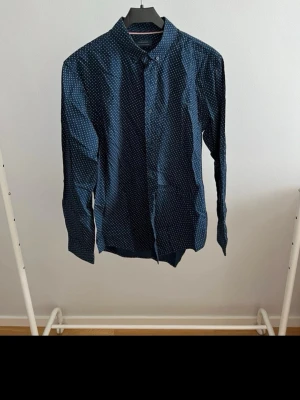 Mörkblå slim fit skjorta Zara Man - Snygg mörkblå skjorta från Zara Man med små vita och röda prickar. Slim fit-modell med klassisk krage och knappar framtill. Perfekt för dig som gillar stilrena detaljer och en smalare passform.