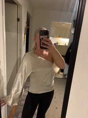 Champagnefärgad oneshoulder topp - Snygg champagnefärgad oneshoulder topp med lång, vid ärm och glansigt material. Köpt på Ginatricot, storlek L men sytt in midjan så idag en storlek M!