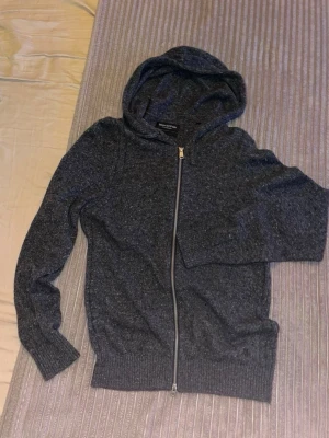 Mörkgrå italiensk ull ziphoodie med dragkedja från Marc’o polo - Mysig mörkgrå hoodie från Marc o polo med hel dragkedja framtill och ribbade muddar vid ärmslut och nederkant. Tillverkad i ett mjukt italienskt ull material och har en klassisk huva. Perfekt för en avslappnad och stilren look. 