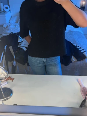 Svart stickad topp med kort ärm - En svart stickad topp med korta ärmar och rund hals. Toppen har en loose passform och är enkel att matcha till olika outfits. Perfekt för dig som gillar en stilren och enkel look.
