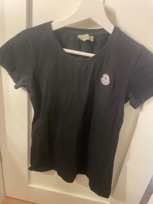 Svart t-shirt från Moncler - En svart t-shirt från Moncler med rund halsringning och korta ärmar. T-shirten har en liten Moncler-logga på bröstet och är tillverkad i mjuk bomull. Enkel och stilren design som passar till det mesta. Inget kvitto finns tyvärr men köpt på NK