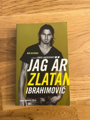 Jag är Zlatan Ibrahimović bok - Självbiografi med gul och svart framsida, skriven av Zlatan Ibrahimović tillsammans med David Lagercrantz. Omslaget har ett porträtt i svartvitt och tydlig text. Boken är tryckt på papper och har mjuka pärmar.