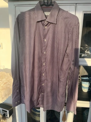 Rutig skjorta från Eton slim fit - Säljer en snygg rutig skjorta från Eton i slim fit-modell. Skjortan har små rutor i lila och vitt, klassisk krage och knappar framtill. Perfekt för dig som gillar stilrena detaljer och vill ha en skjorta som sticker ut lite extra. OBS! Hals storlek 16(41)  slim 