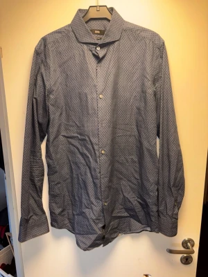 Blå mönstrad skjorta från Canclini - Snygg blå skjorta från hugo bossmed diskret geometriskt mönster. Skjortan har klassisk krage, långa ärmar och knäppning framtill. Tillverkad i mjuk bomull som känns skön mot huden. Perfekt för dig som gillar stilrena detaljer.