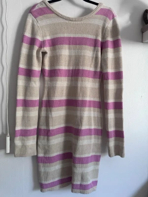 Randig stickad klänningen från Bubbleroom - Mysig stickad klänning med breda beige och lila/rosa ränder. Modellen är långärmad och har en rak, kroppsnära passform. Perfekt för dig som gillar en enkel men färgglad stil. Materialet är mjukt och stretchigt, vilket gör den bekväm att bära hela dagen. ✨ Använd enstaka gånger. Säljs då jag aldrig riktigt använder den.