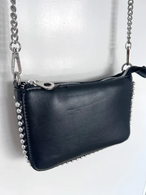 Svart it-girl Y2K axelremsväska med kedja & studs, ny  - Mindre axelremsväska med kedjerem i silver och studsdetaljer - 00s baddie/it-girl känsla!!  Smidig storlek – rymmer mobil, kort & läppglans. Bandet kan kortas lite genom att fästa det som på sista bilden! Statement piece som lyfter hela outfiten.