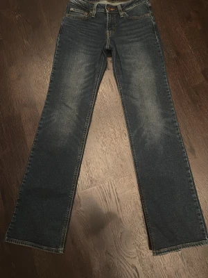 Superlow Bootcut jeans blå 24 - Säljer ett par blå Superlow Bootcut jeans i storlek 24. Jeansen har klassisk femficksdesign, låg midja och lätt utsvängda ben. Snygg tvätt med slitningar framtill och kontrastsömmar. Perfekta för en avslappnad och trendig look.