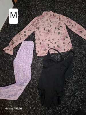 Blommig pyjamaströja & lila byxor M - Säljer ett mysigt pyjamas-set med en långärmad rosa tröja med blommönster och matchande lila byxor med grafiskt mönster. Perfekt för chillkvällar hemma. Inkluderar även ett svart linne med smala axelband.
