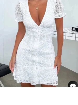 Student klänning Vit spets - Supersöt vit kortklänning i spets med v-ringning och dekorativa knappar framtill. Klänningen har korta ärmar med volangkant och figurnära passform. Min student klänning använt 1 gång🌸