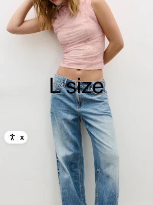 Ljusrosa ärmlös croppad topp - Säljer en ljusrosa croppad topp med diskret blommigt mönster. Toppen är ärmlös och har en tight passform med hög hals. Perfekt att styla med jeans eller kjol för en trendig look.