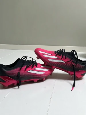 Adidas rosa fotbollsskor med dobbar - Snygga fotbollsskor från Adidas i en skarp rosa färg med svarta detaljer och vita ränder på sidorna. Skorna har klassisk snörning, låg profil och dobbar för bra grepp på planen. Ovandelen är i syntetmaterial som ger lätt känsla och bra bollkontroll.