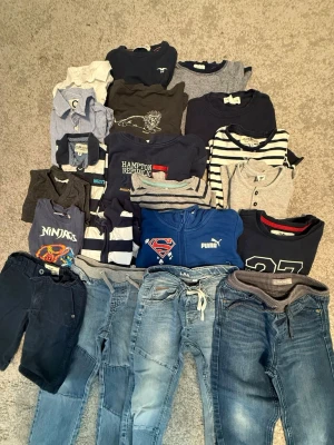 Stort klädpaket pojke, blandade märken - Säljer ett stort klädpaket för pojke med flera tröjor, t-shirts, skjortor och jeans i olika blå, grå och vita nyanser. Märken som Puma, Hampton Republic och Superman finns med. Plaggen har olika mönster som ränder och tryck, och materialet är främst bomull och denim.