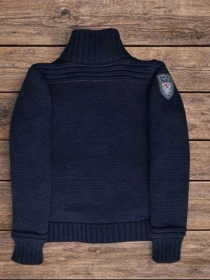 Mörkblå stickad tröja från N.Z.A - Säljer en mörkblå stickad tröja från N.Z.A med hög krage och ribbade muddar. Tröjan har ett snyggt märke på vänster ärm och knäppning framtill. Materialet är grovstickat och ger en cool och avslappnad look. Hör bara av er vid minsta fundering. Priset är inte hugget i sten.