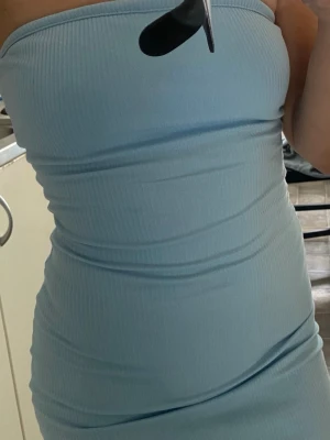 Ljusblå ribbad tubklänning med slits - Trendig ljusblå tubklänning i ribbad bomullsmix med en hög slits på sidan. Klänningen är figurnära och ärmlös, perfekt för sommarens alla tillfällen. Enkel och stilren design som ger en fräsch look.