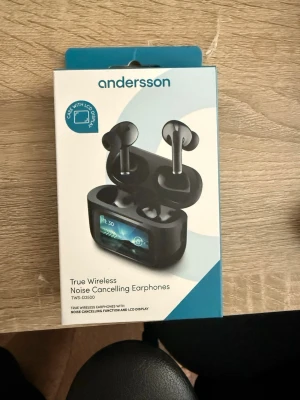 Andersson trådlösa hörlurar med LCD - Säljer ett par svarta Andersson True Wireless Noise Cancelling Earphones (TWS-D2500) med laddningsetui som har LCD-display. Hörlurarna är in-ear-modell och har brusreducering samt modern design i plast. Perfekt för dig som vill ha trådlös frihet och snygg look.