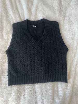 Svart stickad väst med v-ringning - Snygg svart stickad väst med v-ringad hals med och ribbade kanter med mjuk och bekväm passform, från Lindex.  Perfekt att bära över en skjorta eller t-shirt till skolan eller vardags. Enkel att styla med olika outfits 