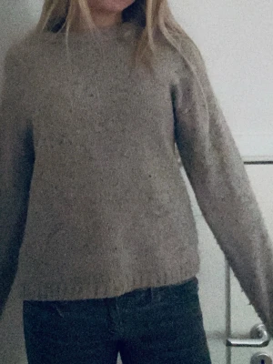 Beige stickad tröja med rund hals - Mysig beige stickad tröja med rund hals och långa ärmar. Tröjan har en enkel, klassisk design med ribbstickade muddar vid ärmslut och nederkant. Perfekt för lager på lager och passar till det mesta i garderoben.