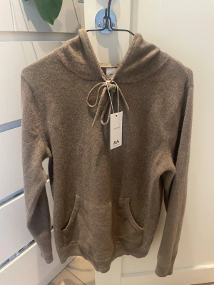 Kashmir hoodie John Henric - Mysig beige/brun hoodie från John Henric i mjuk kashmir. Klassisk modell med huva, känguruficka framtill. I nyskick använd 1-2 gånger.