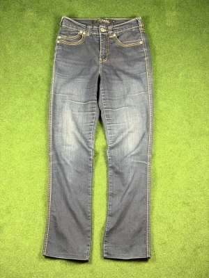 Blå bootcut jeans från Magic - Snygga blå bootcut jeans från Magic med kontrastsömmar och klassisk femficksdesign. Jeansen har dekorativa nitar och slitningar framtill för en cool look. Tillverkade i mjukt denimtyg som sitter skönt hela dagen.