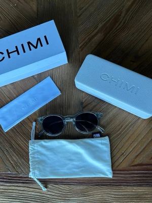 Transparenta solglasögon från CHIMI - Snygga solglasögon från CHIMI med transparent båge och runda, mörktonade linser. Kommer med originaletui och putsduk. Perfekta för dig som vill ha en clean och modern look.