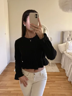 Svart croppad topp  - Snygg svart långärmad topp med croppad passform och volangkant nedtill. Lite liten i storleken så passar 32 och 34 (är storlek 34) 