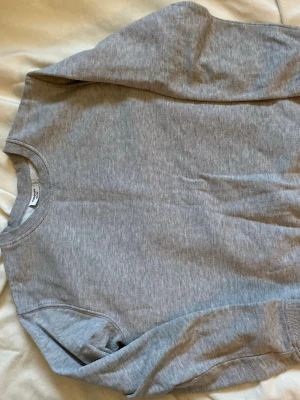 Grå sweatshirt i bomull - En enkel och stilren grå sweatshirt med rund halsringning och långa ärmar. Tillverkad i mjuk bomullsblandning och har ribbade muddar vid ärmslut och nederkant. Perfekt för en avslappnad look.