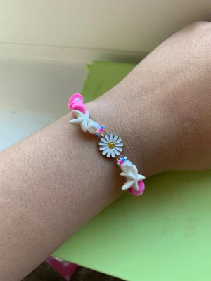 Färgglatt pärlarmband med blomma - Sött armband med vita och rosa pärlor, dekorerat med en stor blomma i mitten och små stjärnformade pärlor. Armbandet har en lekfull och trendig design som passar perfekt för dig som gillar färgglada accessoarer.