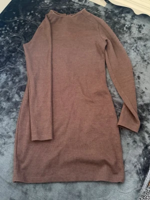 Brun ribbad stickad klänning - Mysig brun stickad klänning med ribbad struktur och lång ärm. Klänningen har en enkel, rak passform och är i kort modell. Perfekt för dig som gillar stilrena och bekväma plagg.