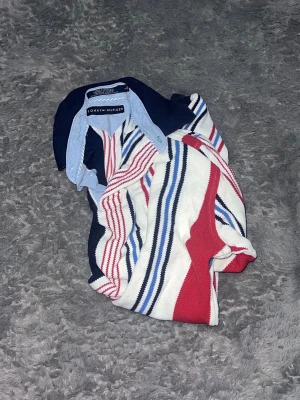 Tommy Hilfiger Vertical Striped Rugby Shirt - Klassisk långärmad pikétröja från Tommy Hilfiger. Tröjan har snygga vertikala ränder och den ikoniska loggan på bröstet. Rejäl och skön kvalitet med snygga detaljer vid kragen och muddar vid ärmsluten. En riktig vintagepärla med en sportig retrolook.  • Skick: Begagnat skick. Det finns en liten fläck på ärmen – vänligen se de sista bildern för en tydlig bild av skicket. 