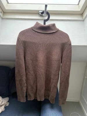 Brun stickad polotröja - Brun stickad polotröja med lång ärm och ribbad krage. Klassisk modell utan synliga detaljer eller mönster.