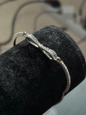 Silverfärgat armband med rosett - Ett elegant armband i silverfärg med en gnistrande rosett dekorerad med små klara stenar. Armbandet har en tunn och smidig kedja som ger en stilren look. Perfekt accessoar för att lyfta din outfit med lite extra bling.